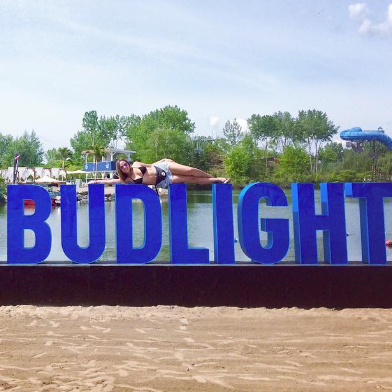 Large blue letters spelling '#LAVIEBUDLIGHT' on a beach with people in the background.