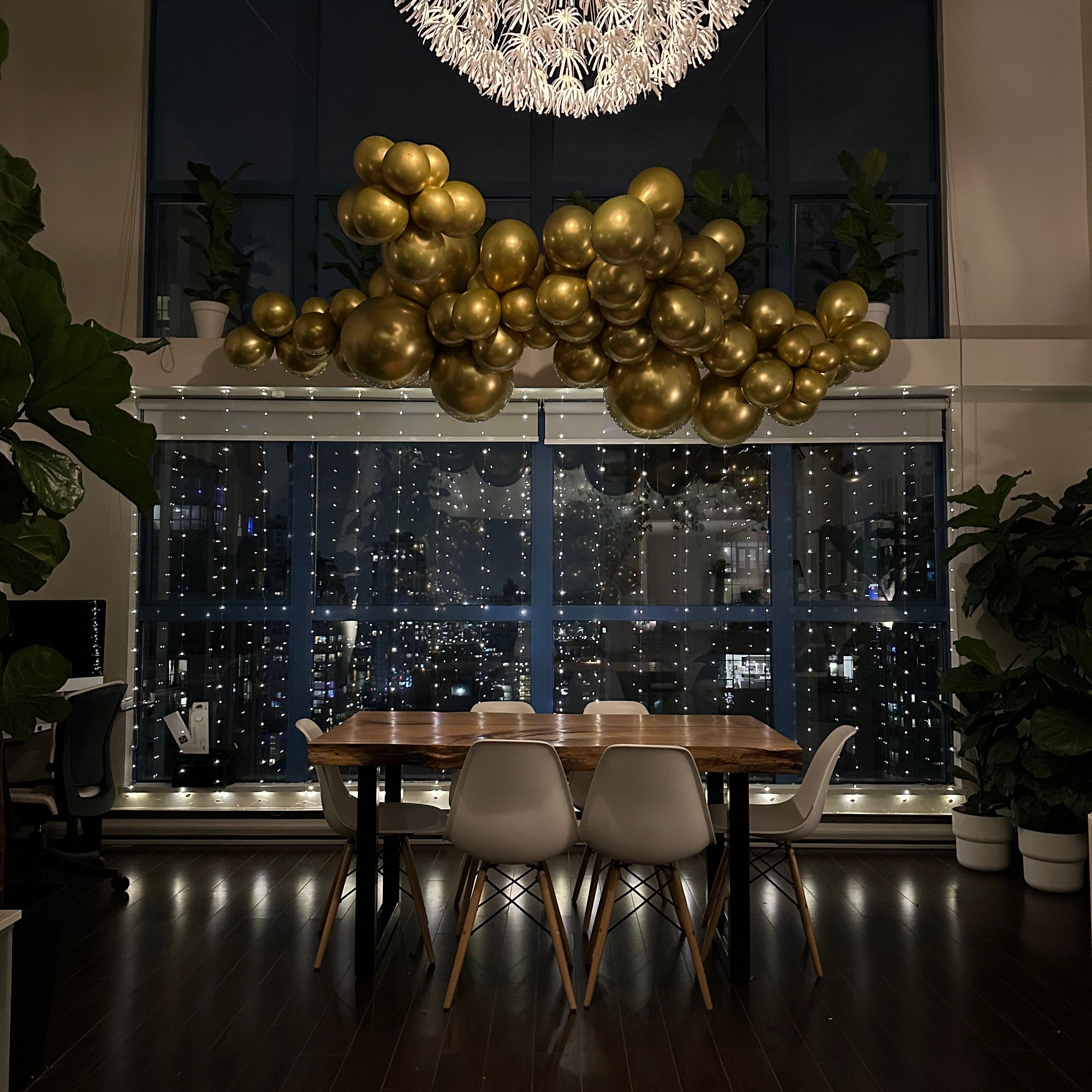 Dining area with gold balloon decorations and a cityscape view from a high-rise window.