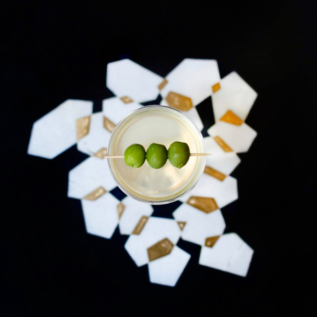 Cocktail with three green olives on a decorative coaster with a black background