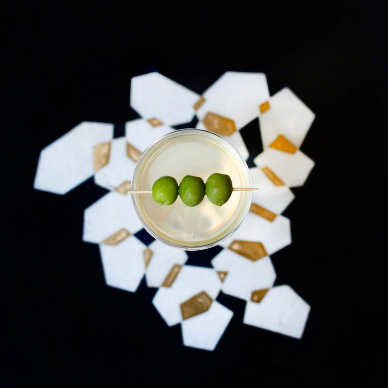 Cocktail with three green olives on a decorative coaster with a black background