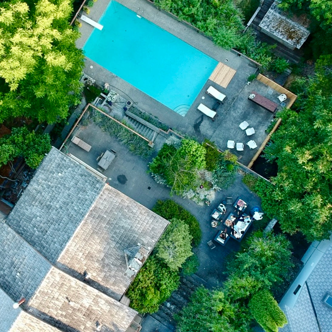 Aerial view of a pool area with lounge chairs and a table surrounded by trees.