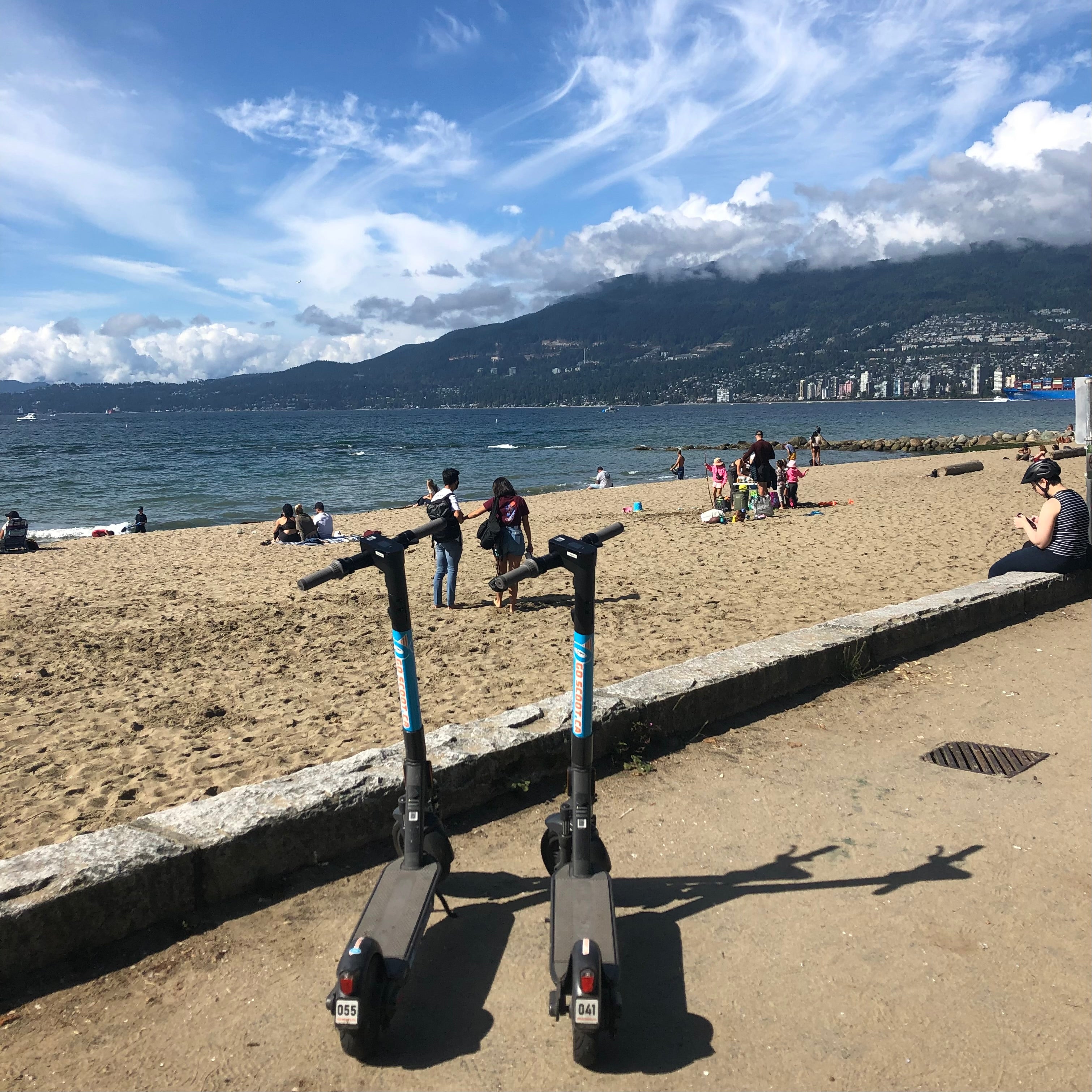 Bike path next to beach with people and mountains in the background