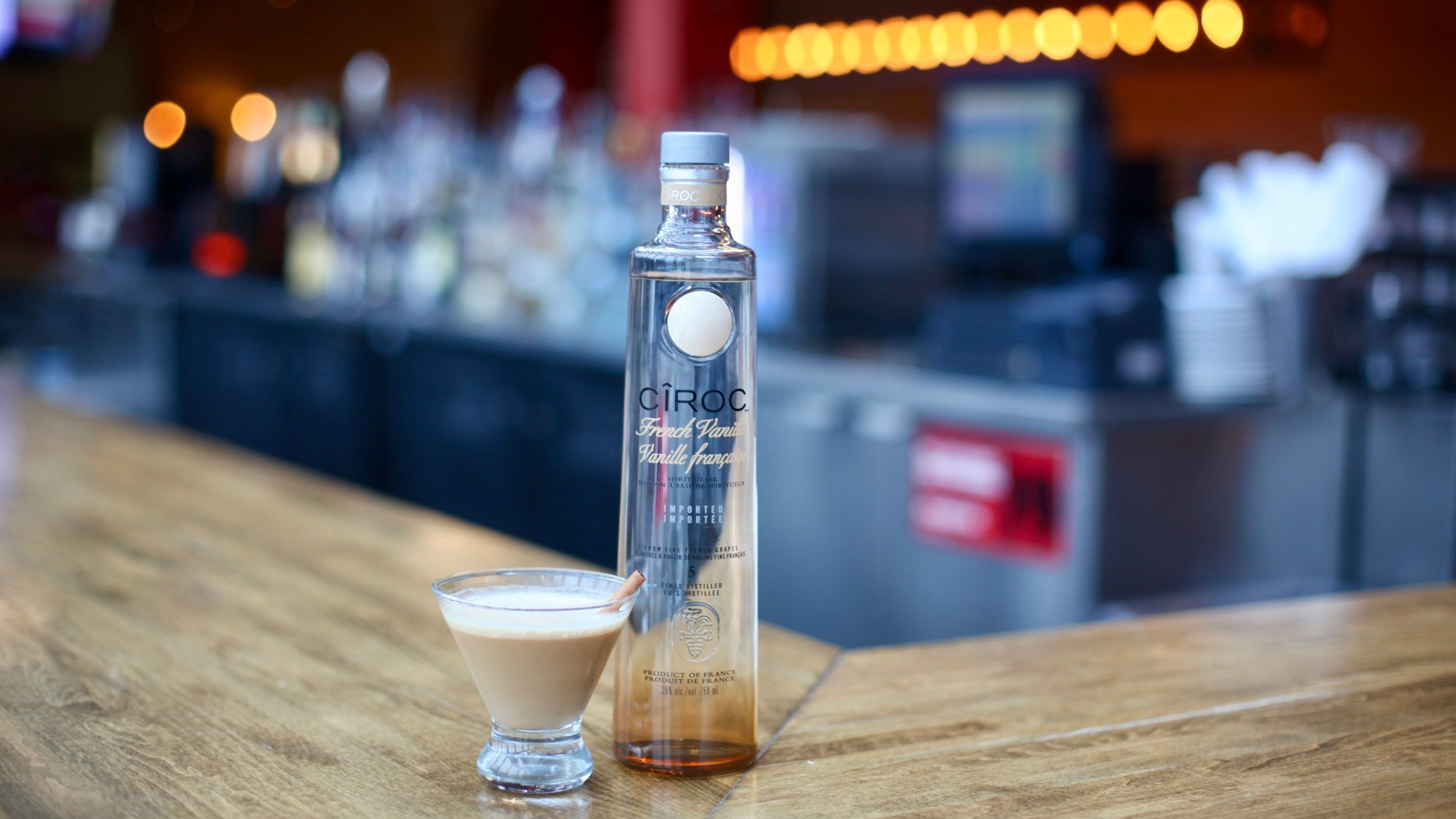 Bottle of Ciroc Vodka on a bar counter with a shot glass filled with a creamy liquid.