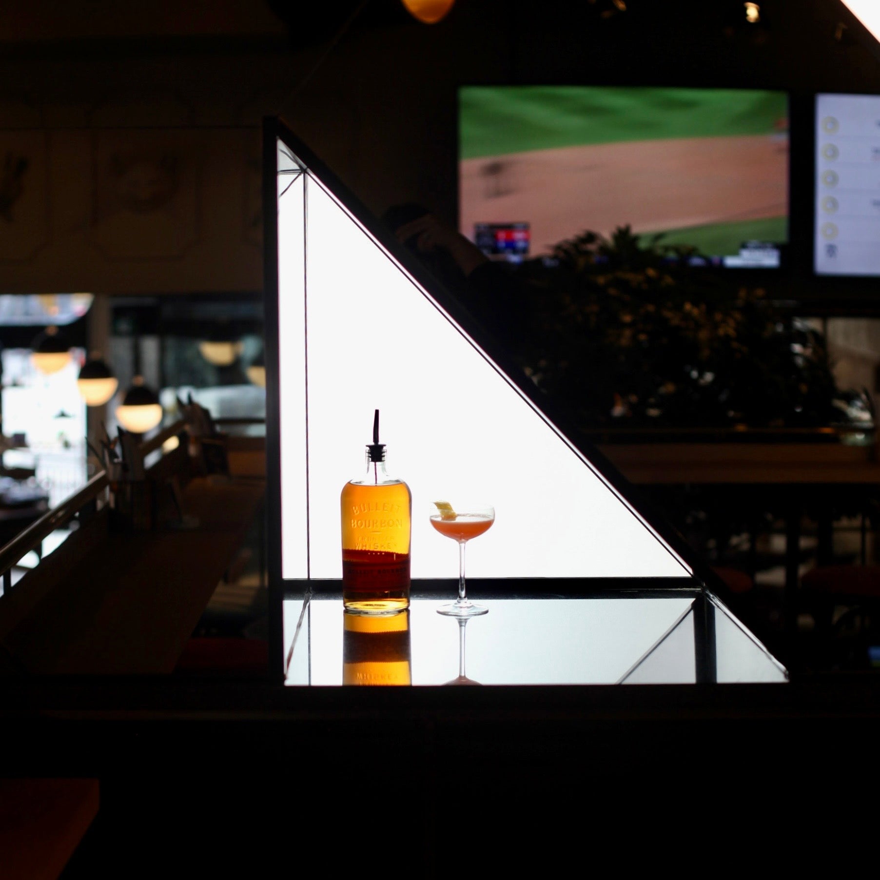 Bottle and glass of cocktail on a reflective surface with a blurred bar background