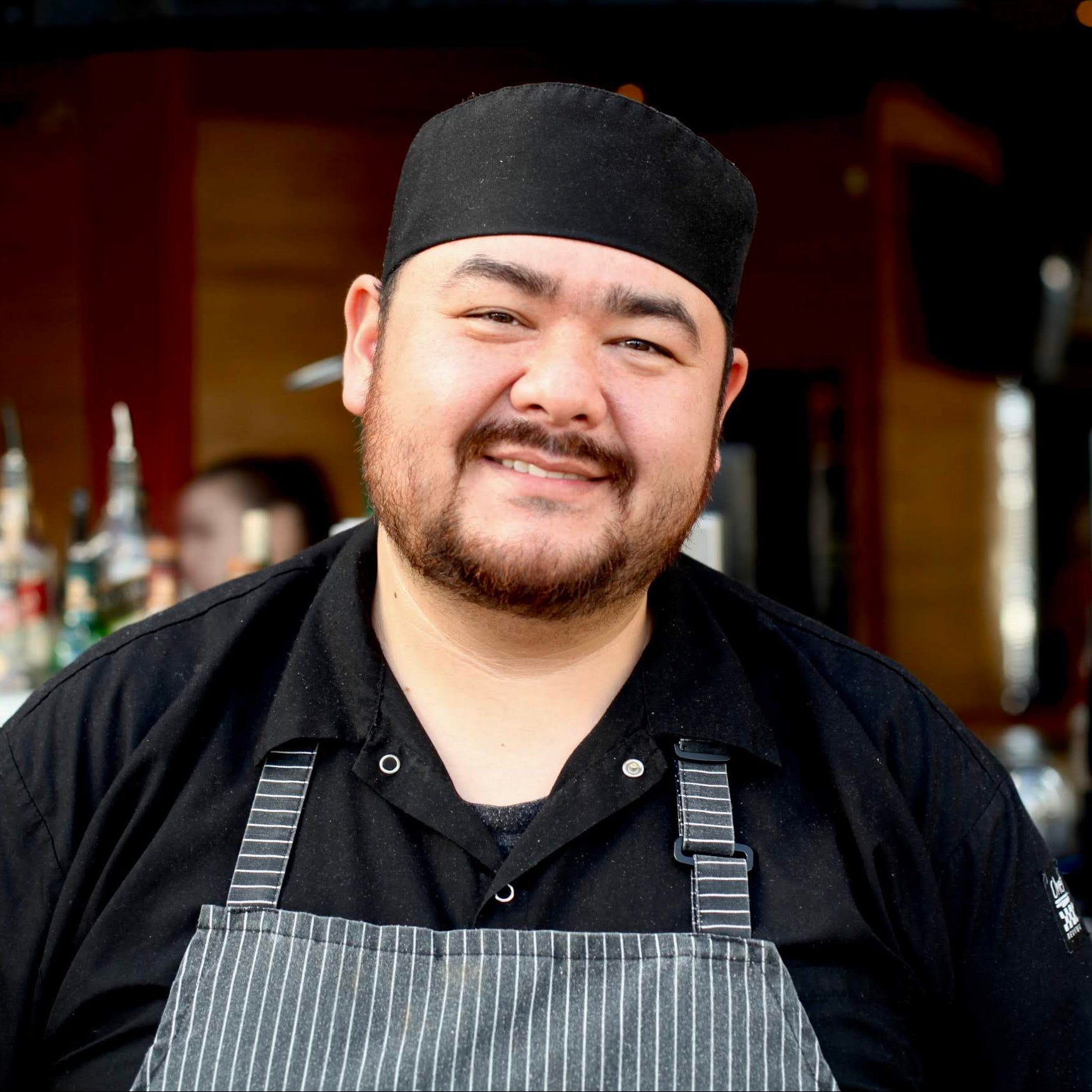 Man wearing a black chef's hat and apron in a kitchen setting