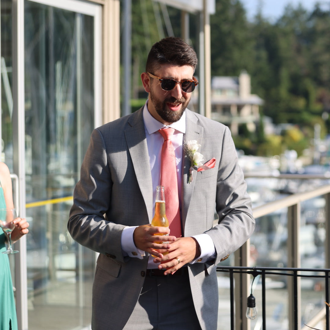 Man in a gray suit with a pink tie holding a beer, standing by a marina.
