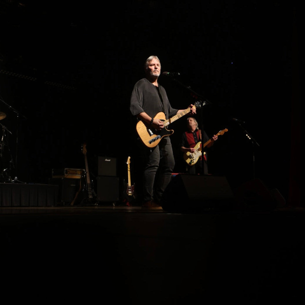 David Martin and another musicians on stage with guitars and a microphone, performing in front of a dark background.