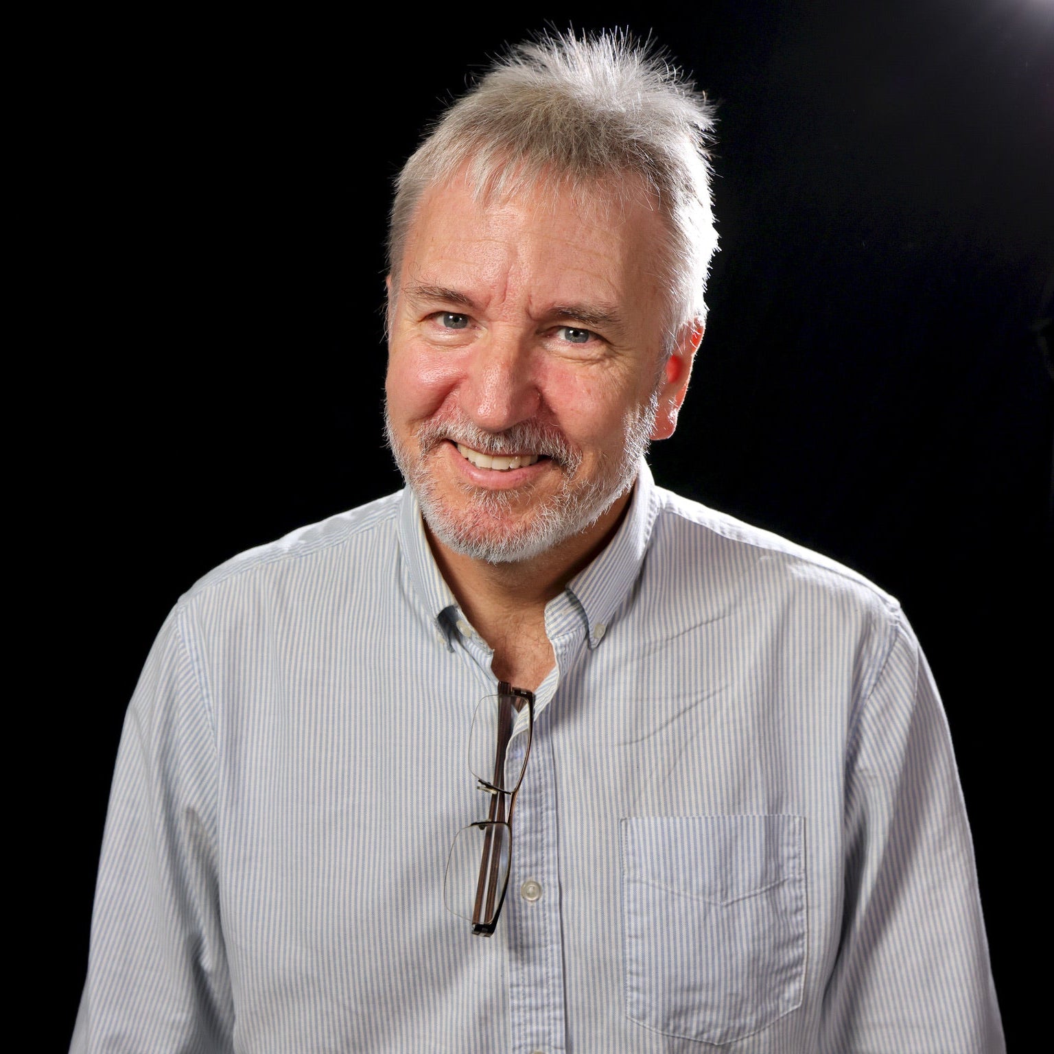 David Martin with gray hair and beard wearing a light blue shirt against a black background