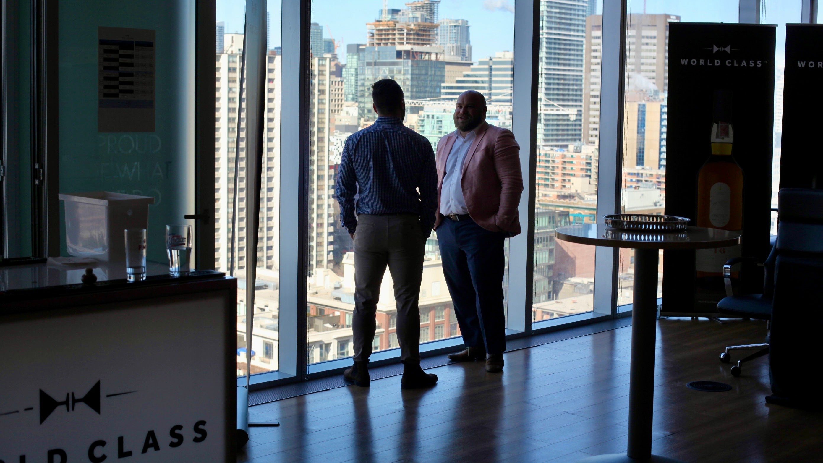 Two men standing in a modern office with large windows overlooking a cityscape.