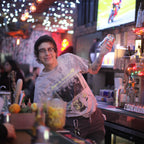 Person behind a bar with festive lights and a TV in the background