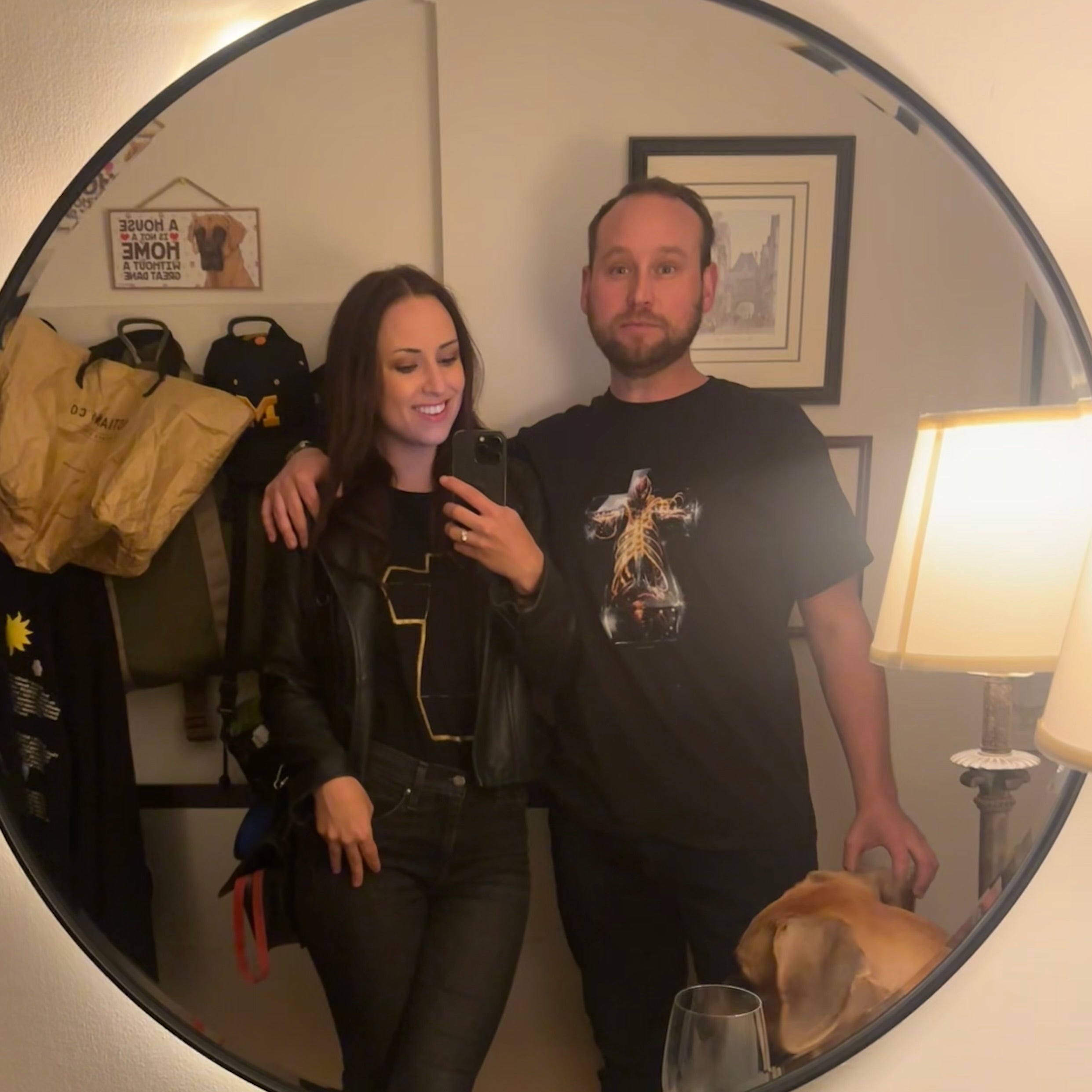 Two people standing in front of a mirror in a room with a lamp and bags.
