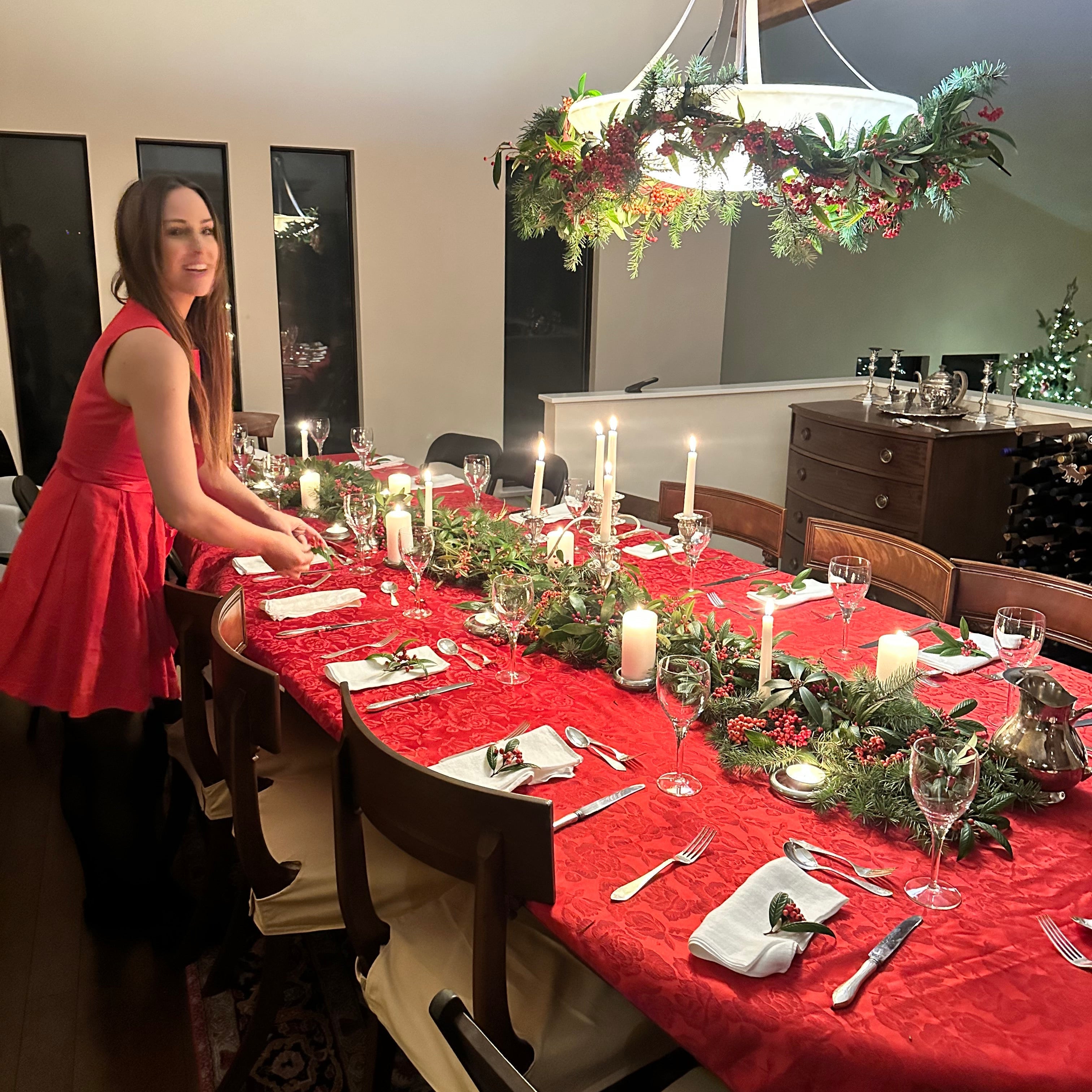Evelyn Martin  in a red dress setting a festive Christmas table with candles and decorations.
