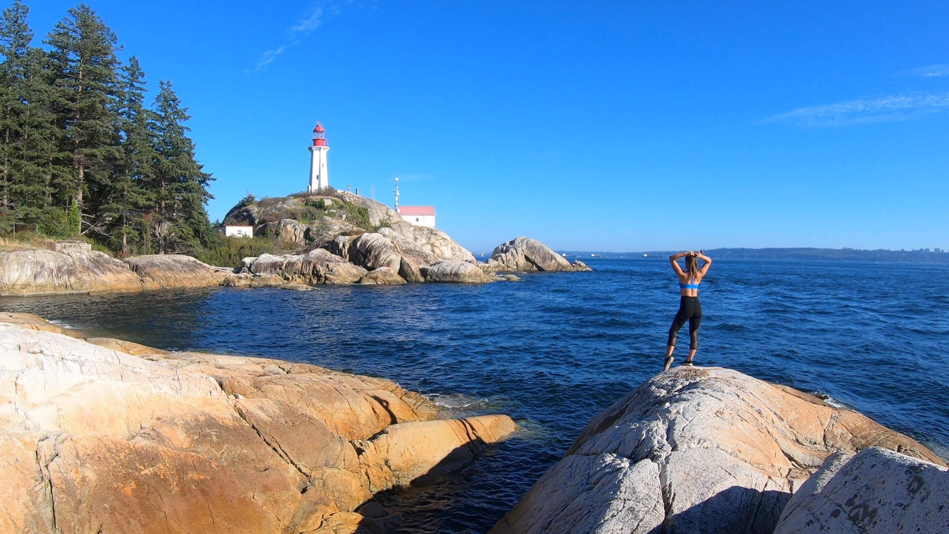 Person standing on a rocky outcrop with a lighthouse in the distance.