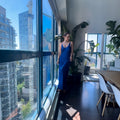 Woman in a blue dress standing by a large window with cityscape view