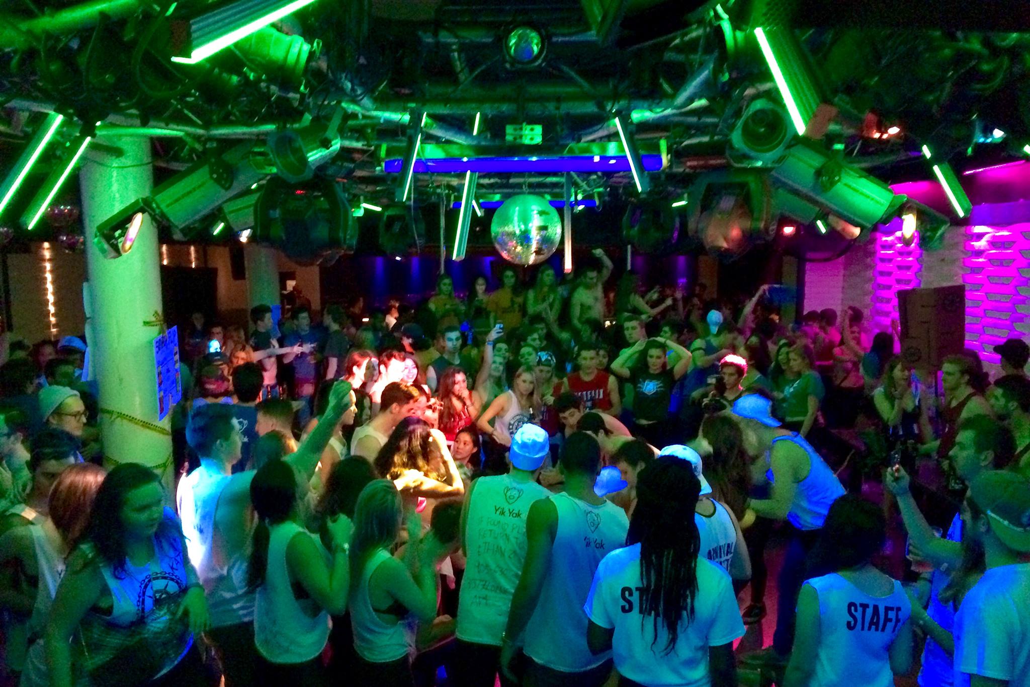 People dancing in a club with colorful lighting and a disco ball.