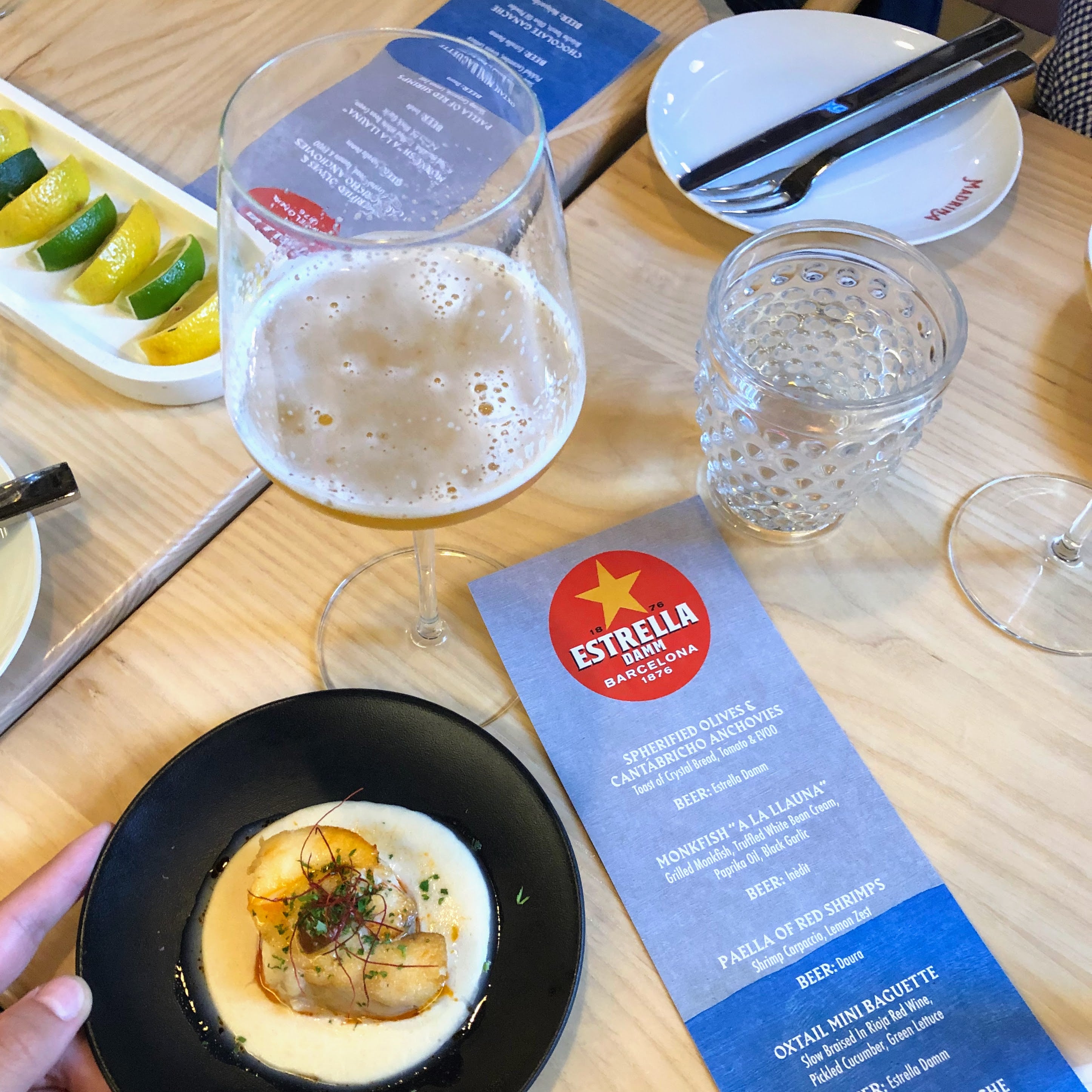 Dinner table with a dish, glass of beer, water glass, and Estrella Galicia menu.