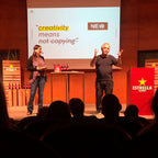 Two people on a stage with a presentation slide about creativity and Estrella Damm branding.