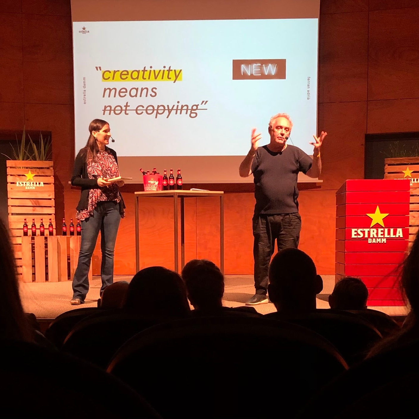 Two people on a stage with a presentation slide about creativity and Estrella Damm branding.