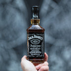 Hand holding a bottle of Jack Daniel's Tennessee Whiskey against a blurred background