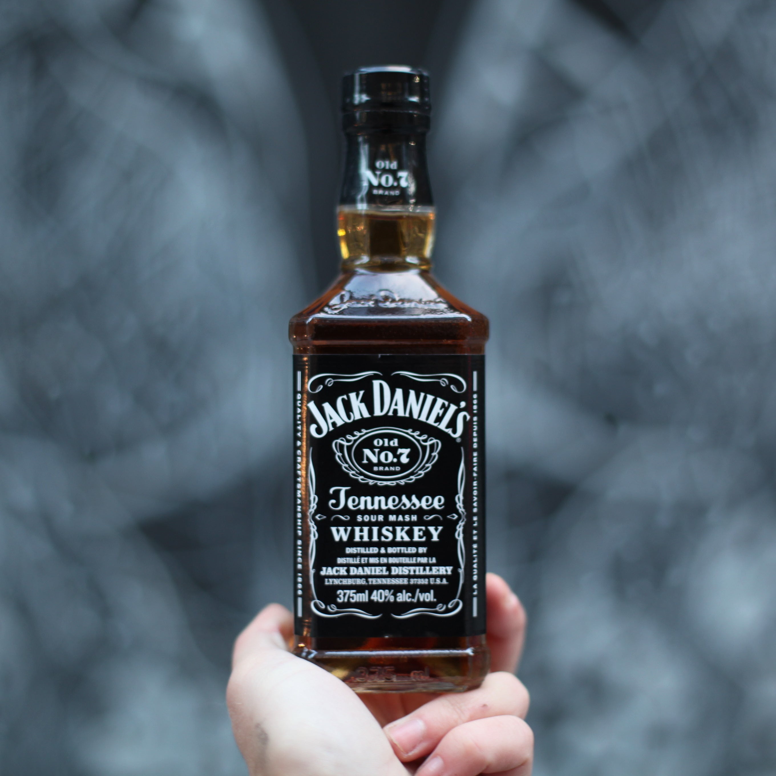 Hand holding a bottle of Jack Daniel's Tennessee Whiskey against a blurred background