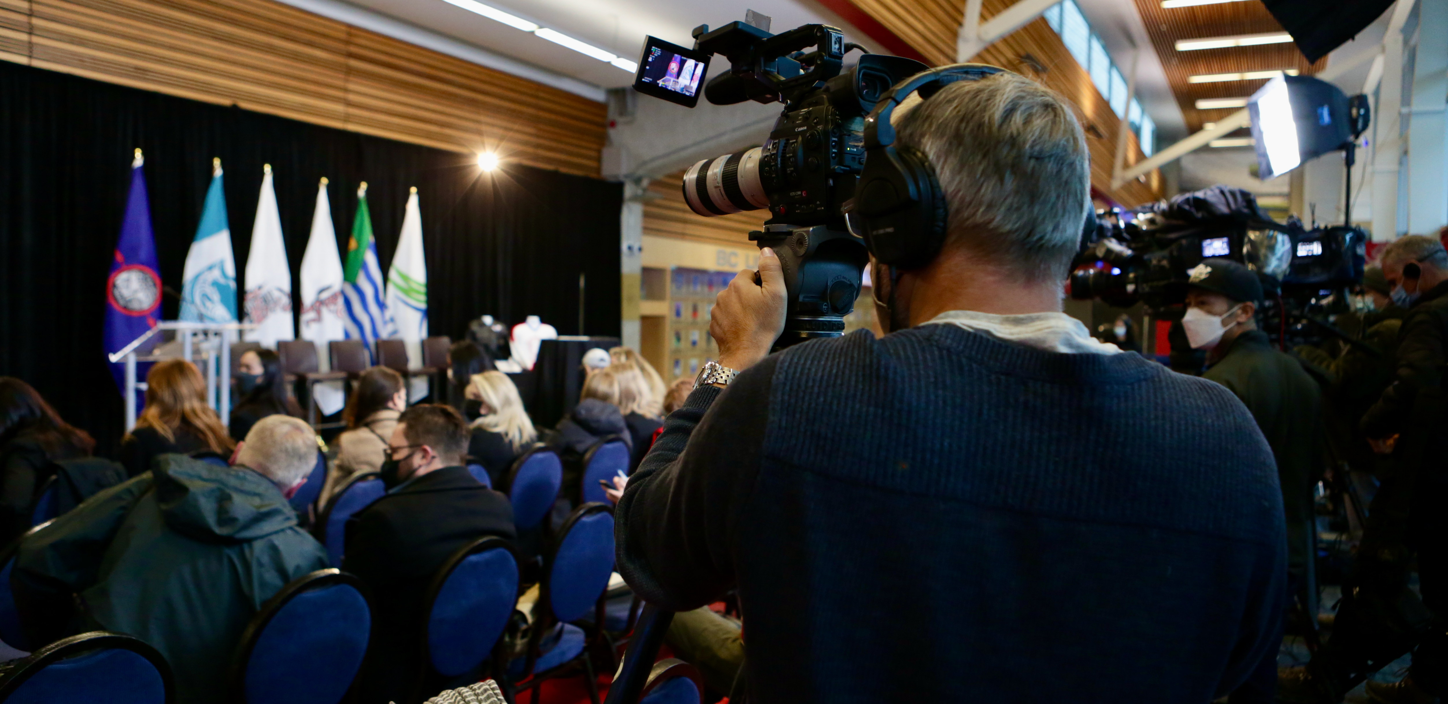 Journalist with camera at a press conference with flags in the background