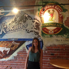 Evelyn Martin standing in front of a wall with various beer brand logos, including Blue, Kokanee, and Alexander Keith's.