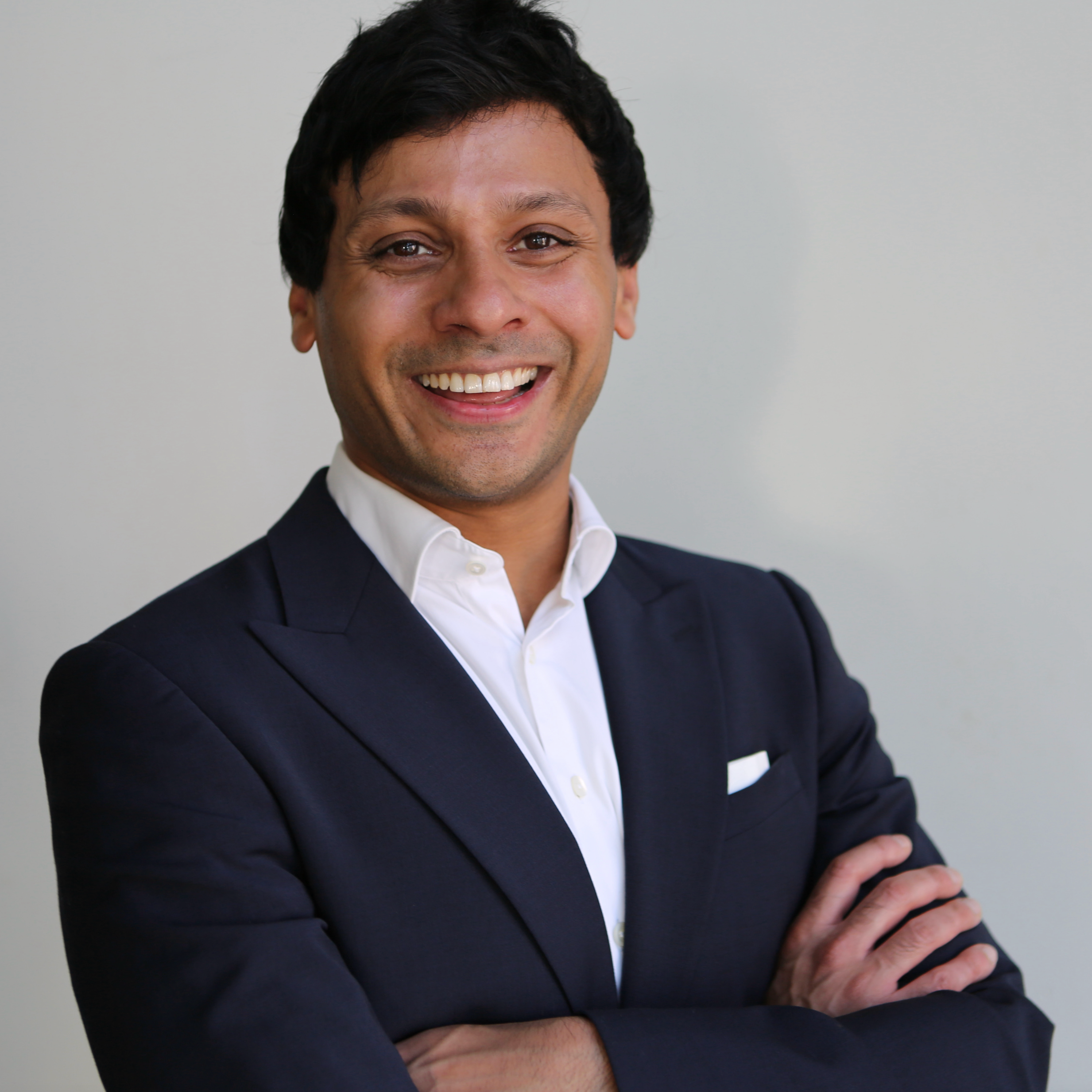 Man in a suit with arms crossed against a plain background