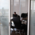 Office interior with people working at desks, glass wall with motivational text.