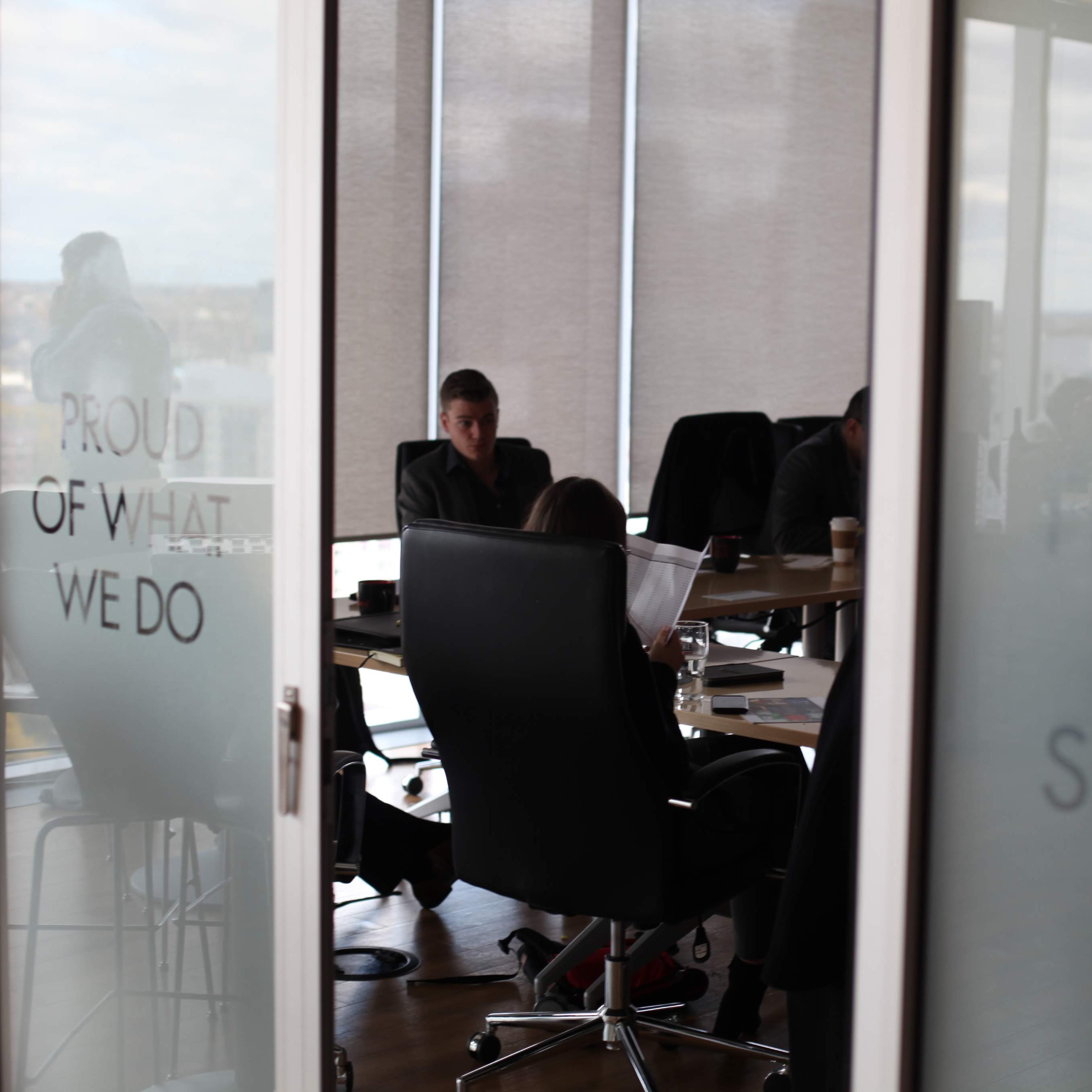 Office interior with people working at desks, glass wall with motivational text.