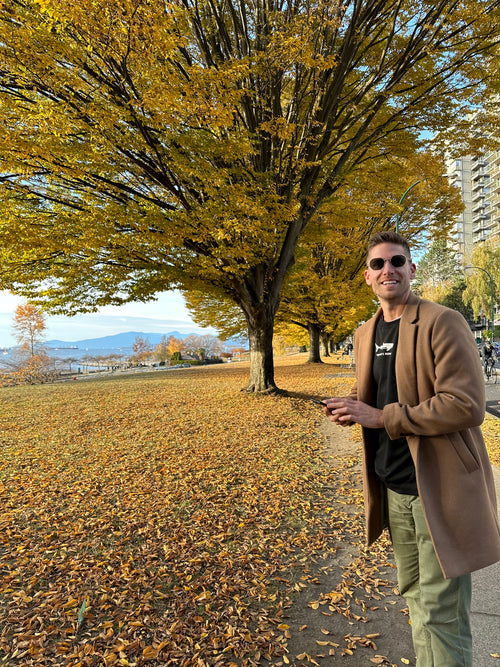 Person standing in a park with trees and a path during autumn.