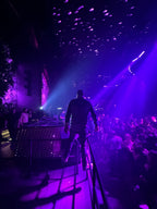 Person on a stage with purple lighting and audience in a dark venue