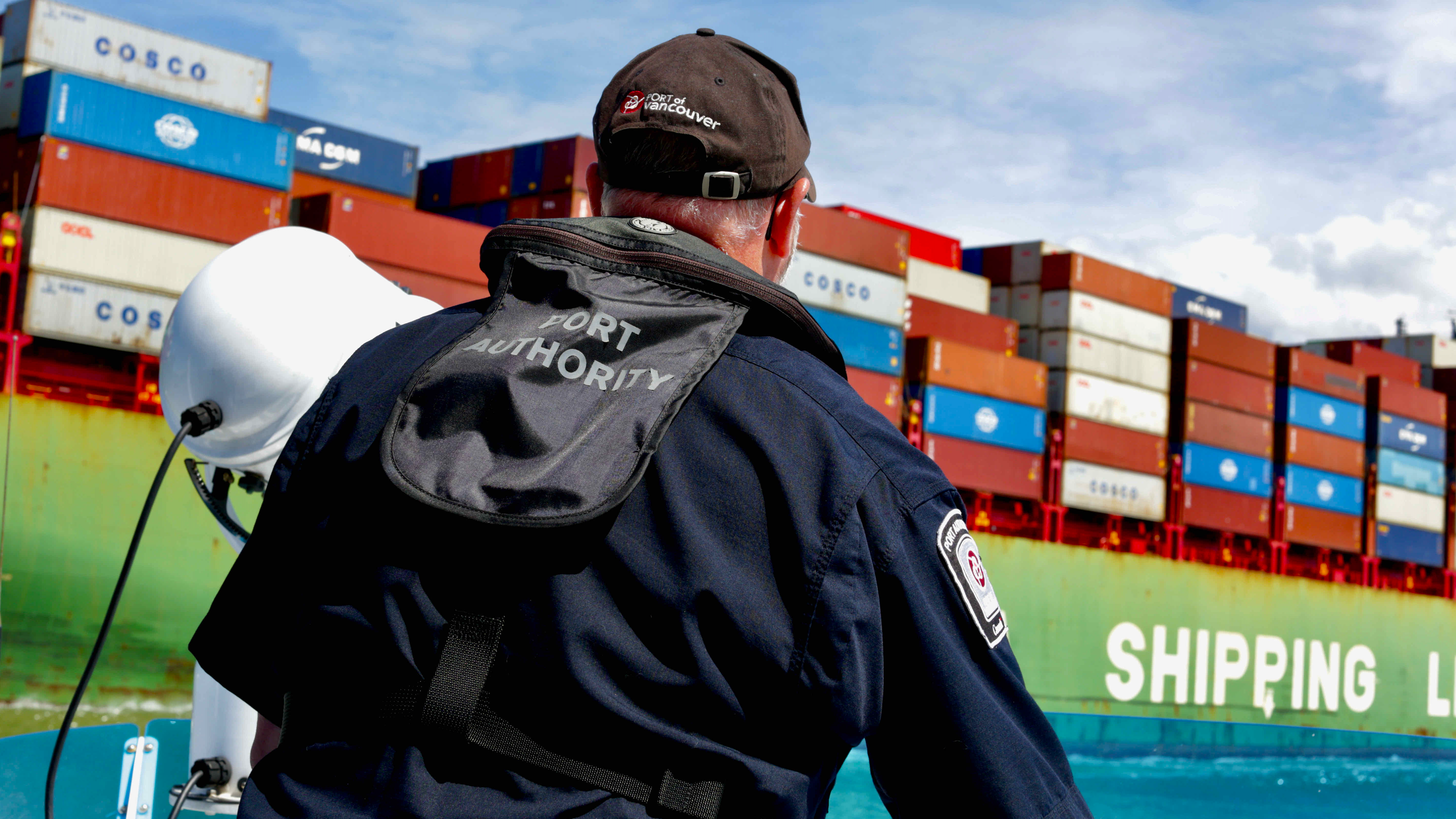 Person wearing a 'Port Authority' jacket in front of shipping containers