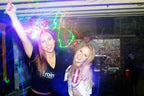 Two people at a party with colorful lights and a crowd in the background