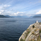 Rocky outcrop overlooking a large body of water with mountains in the background.