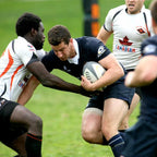 Rugby player in action with ball, surrounded by opponents on a grass field