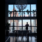 Person standing by a large window with cityscape view, silhouetted against the light