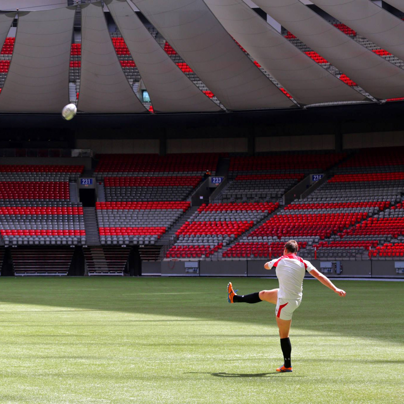 Soccer player kicking a ball on a green field with red seats in the background