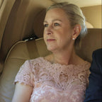 Woman in a pink lace dress sitting in a car with a man in a suit.