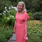 Woman in a pink dress standing in a garden with greenery and flowers.