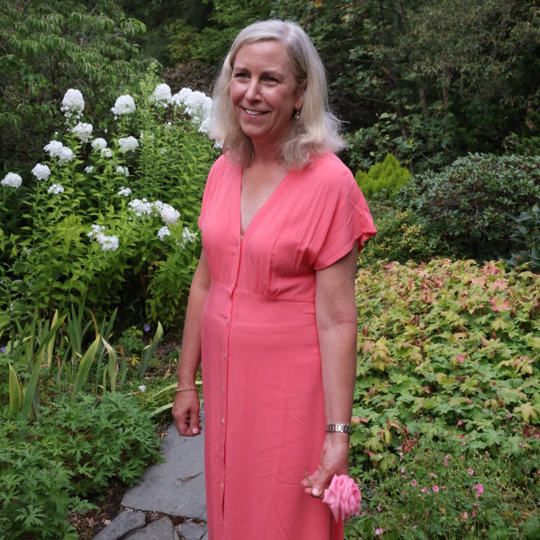 Woman in a pink dress standing in a garden with greenery and flowers.