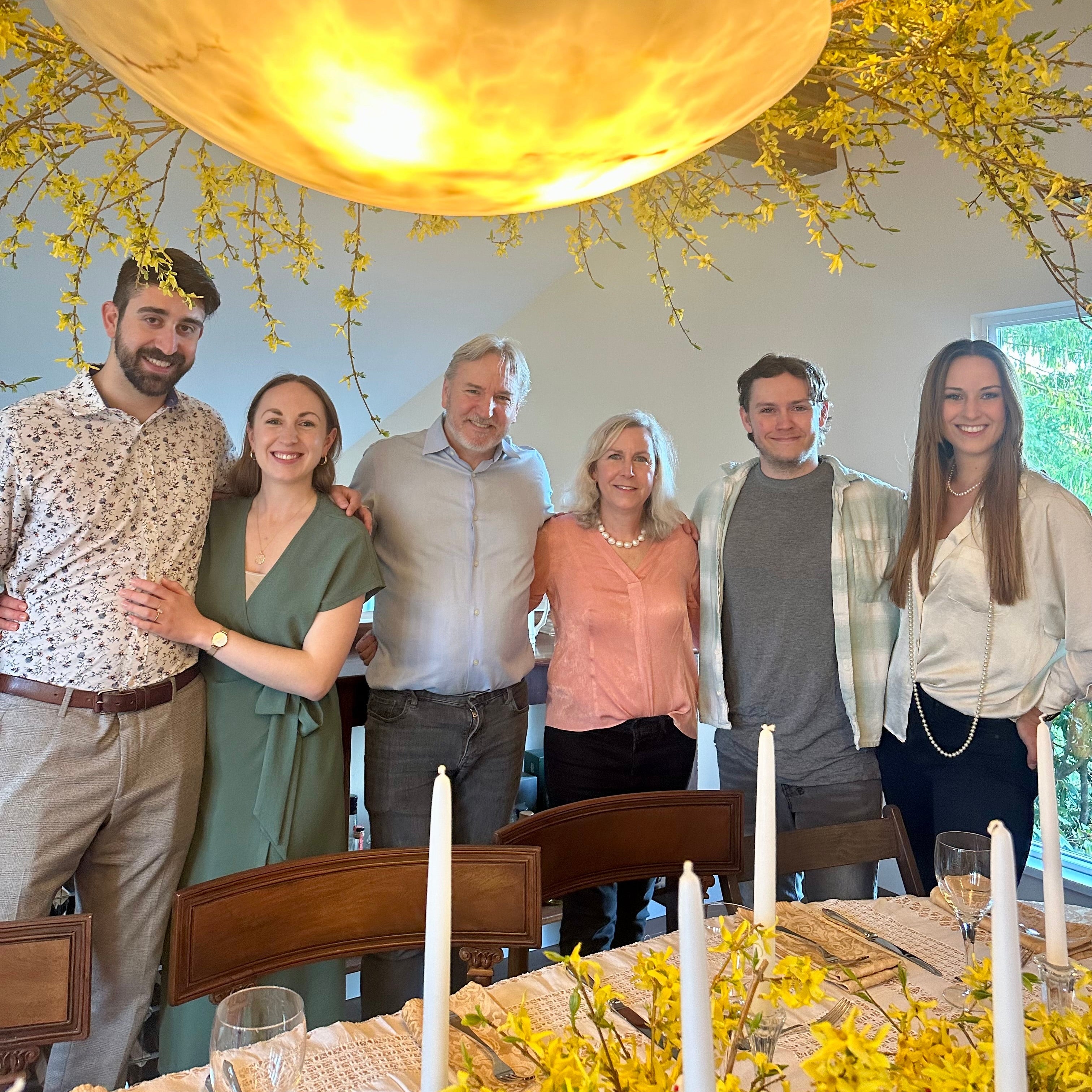 Group of people posing together in a room with a chandelier and floral decorations.