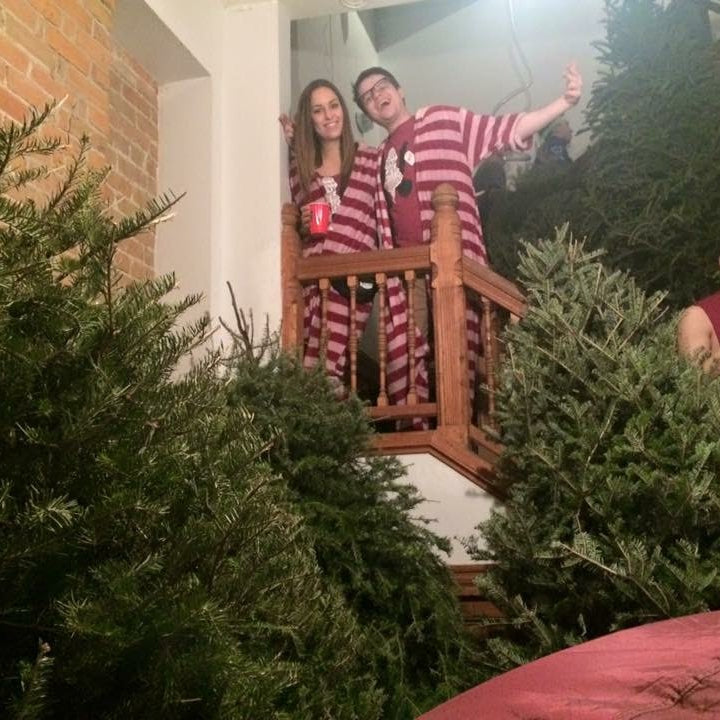 Two people in matching pajama sets standing on a staircase with Christmas trees around.