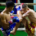Two boxers in a boxing ring with one delivering a kick to the other.