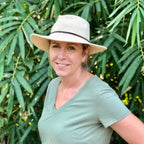 Woman wearing a wide-brimmed hat and green shirt standing in front of green foliage