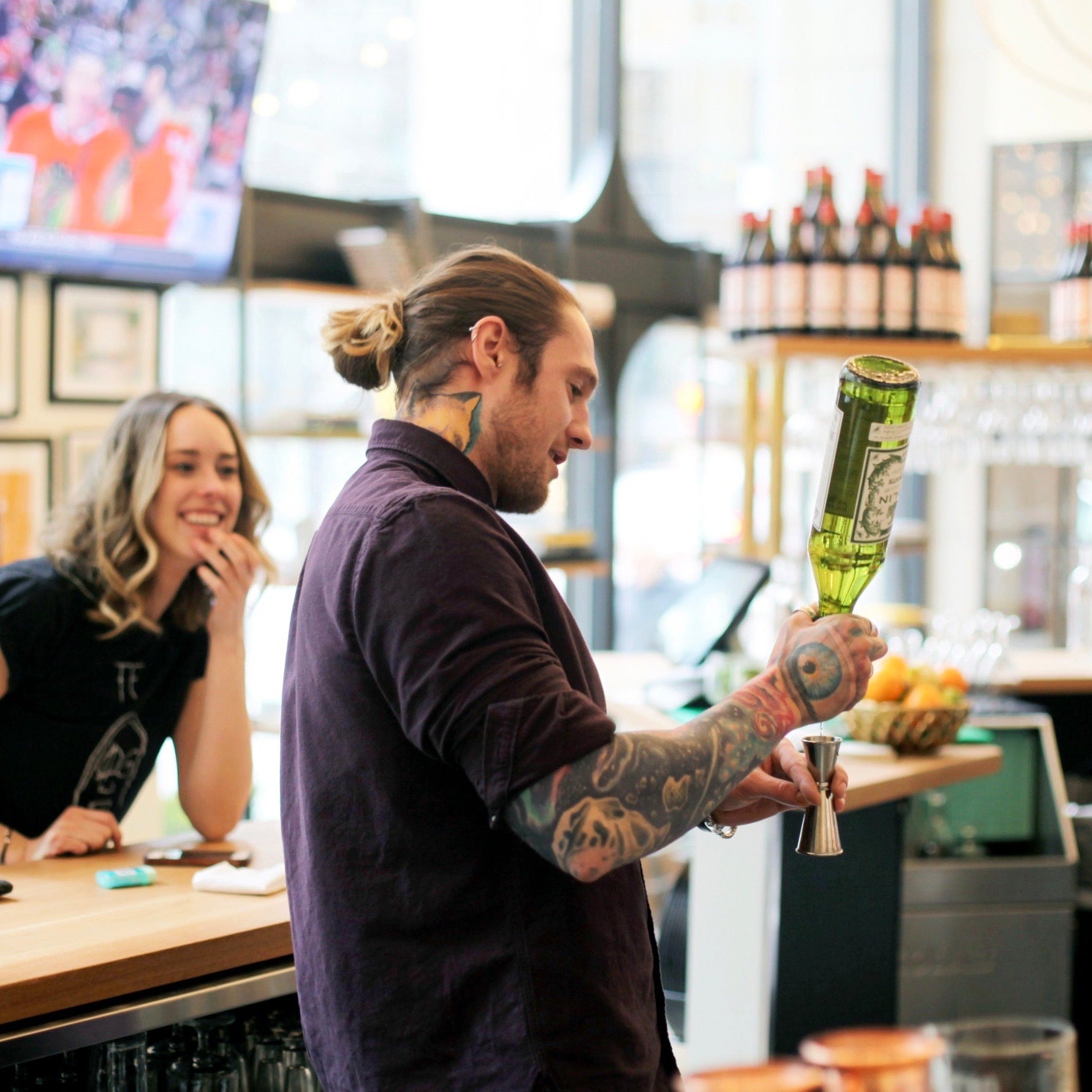 Man preparing a drink at a bar with a woman in the background