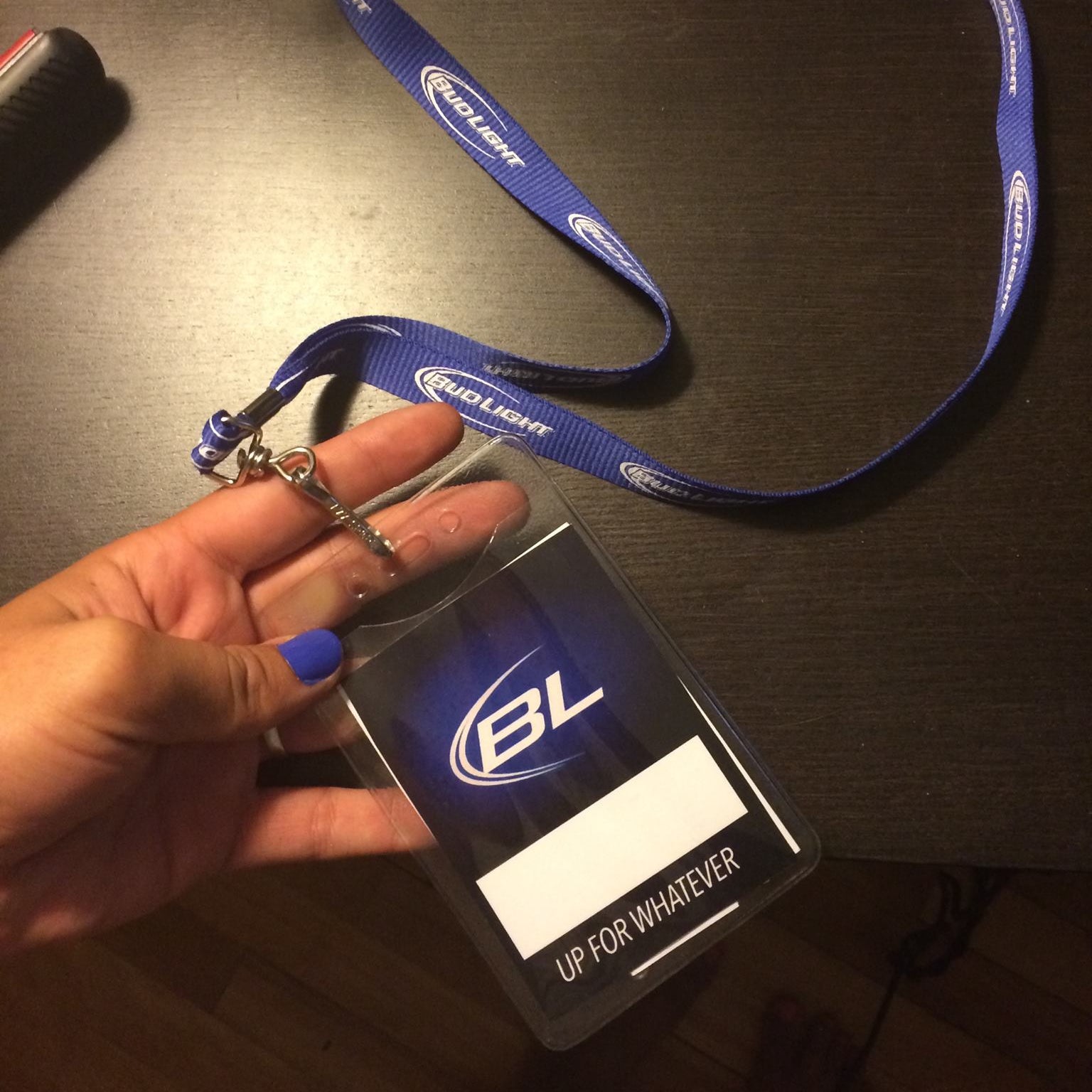 Hand holding a lanyard with a badge featuring a logo on a dark surface