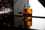 Two bottles of whiskey and two glasses on a bar counter with a blurred bar background.