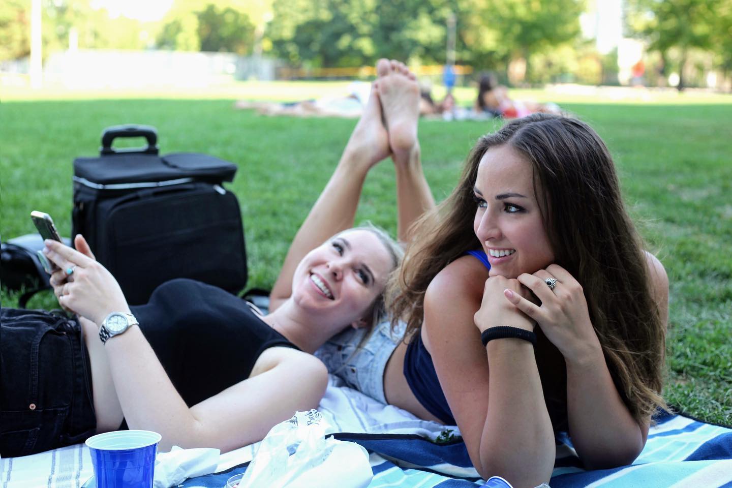 Evelyn Martin lying on a blanket in a park, one using a phone.
