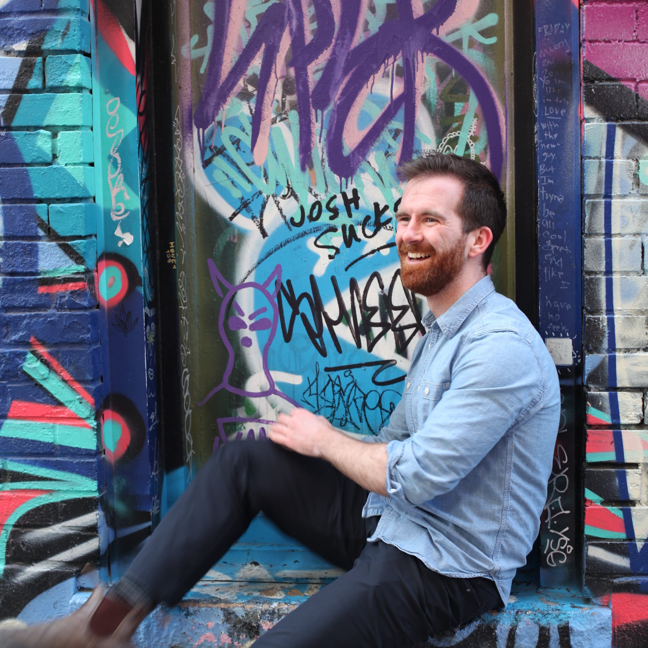 Man sitting against a colorful graffiti-covered wall