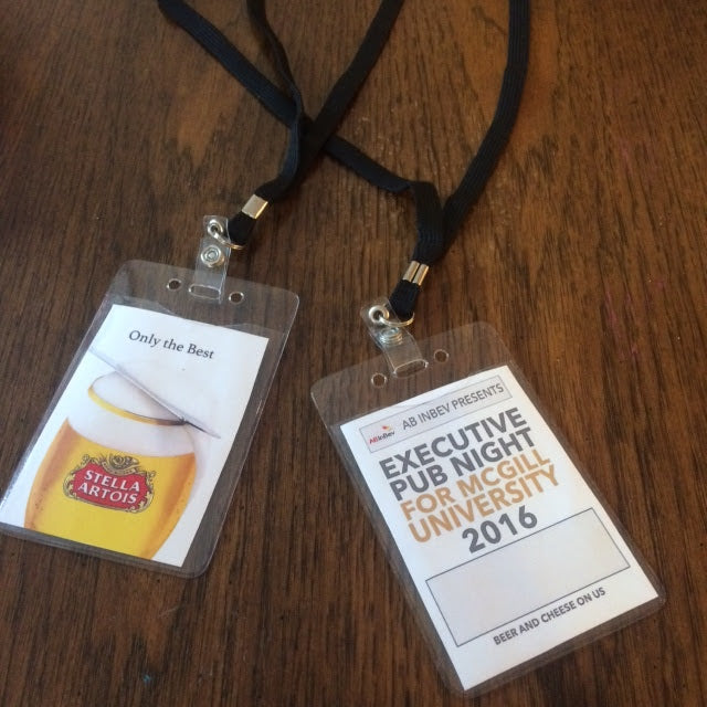 Two name badges on a wooden surface, one with Stella Artois logo and the other with McGill University event details.